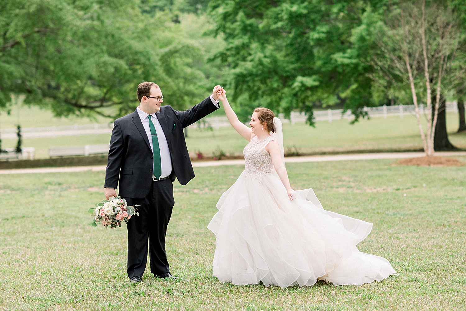groom holds bride hand and twirls her around in field