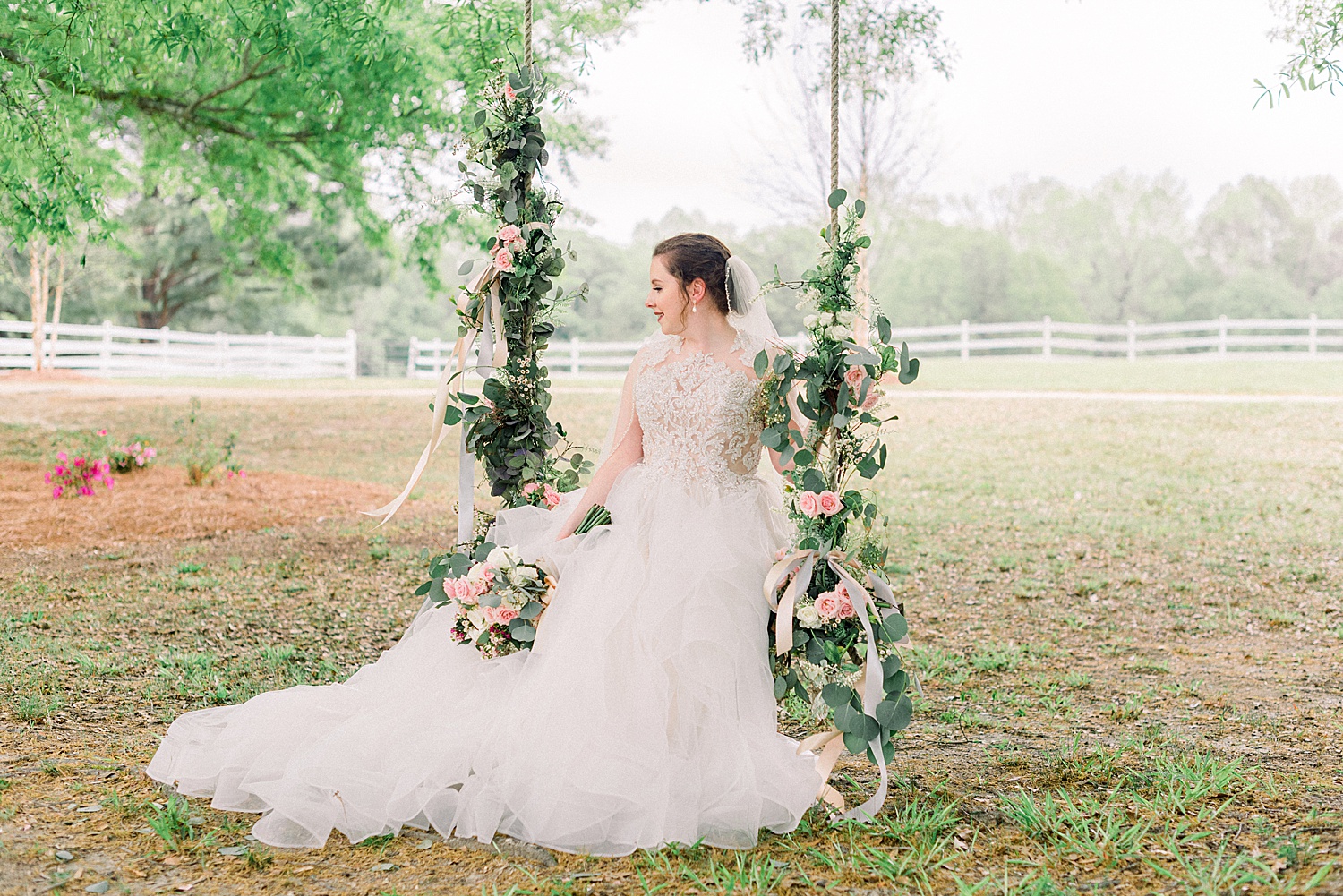 bride sits on decorated swing hanging from tree outside the Tangarray Wedding venue