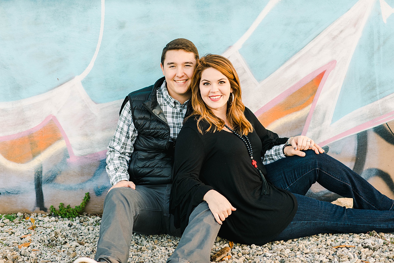 Engaged couple sit against graffiti wall in downtown Birmingham AL engagement session