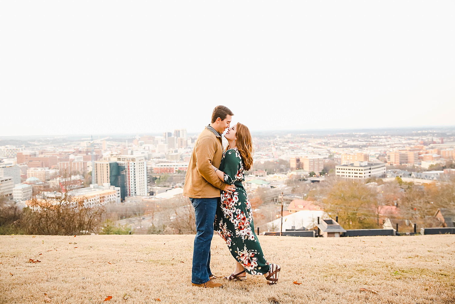 couple kiss standing on hill with the city life in the distance