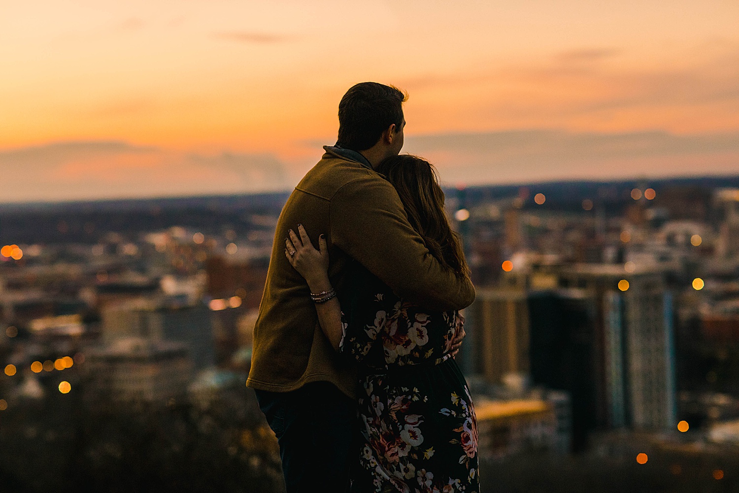engaged couple stand on hill top watching the sunset over Birmingham Alabama
