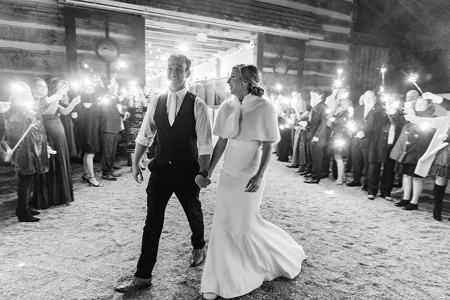 wedding guests hold sparklers as bride and groom walk out of reception