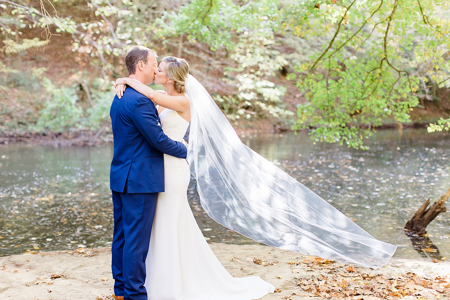 couple kisses while bride's veil is flutters in the wind