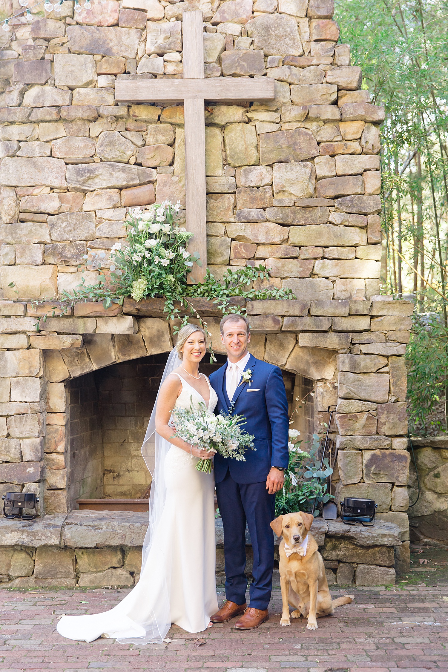 couple stand by stone fireplace with their dog at Swann Lake Stables Wedding