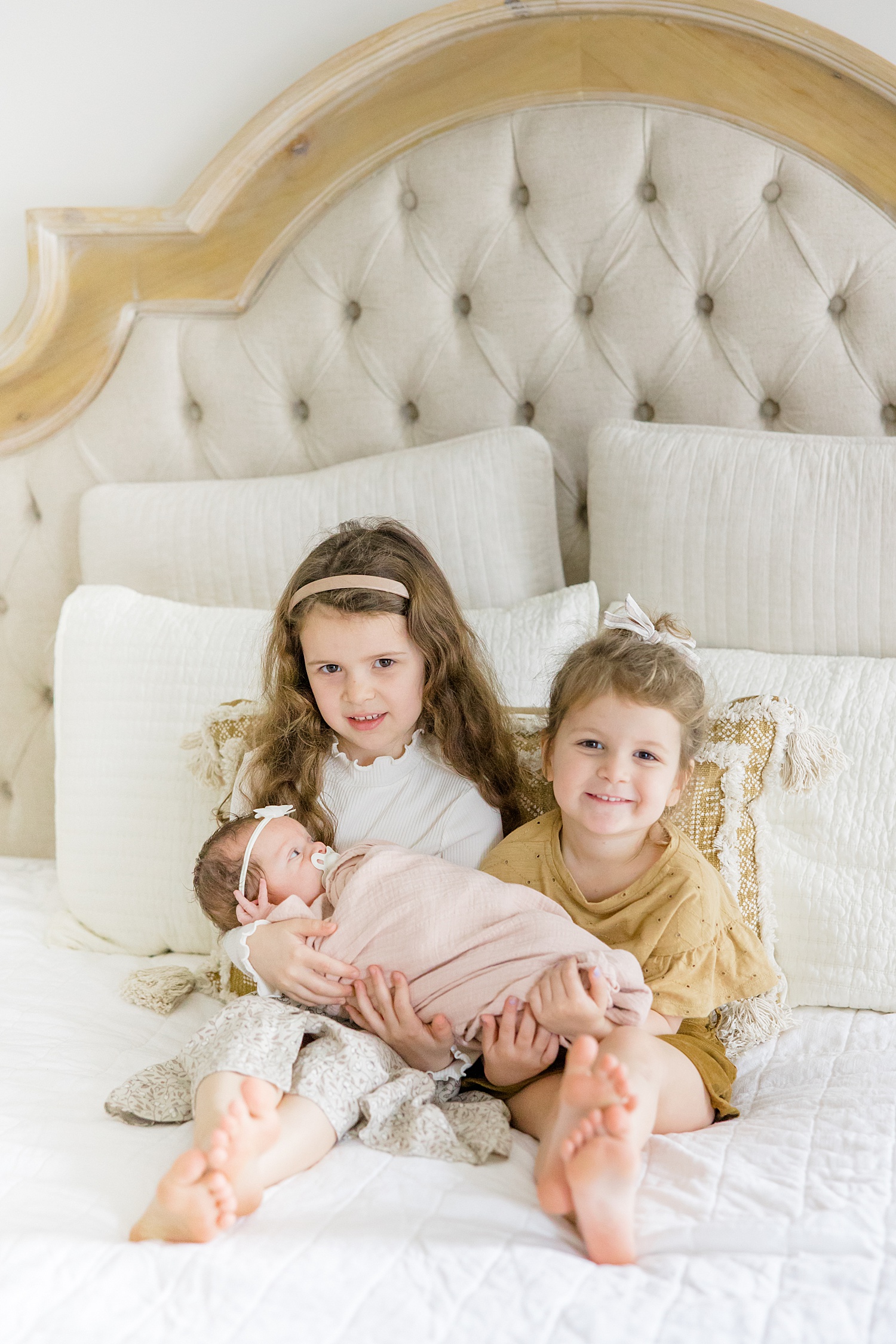 two little girls hold their newborn sister on bed