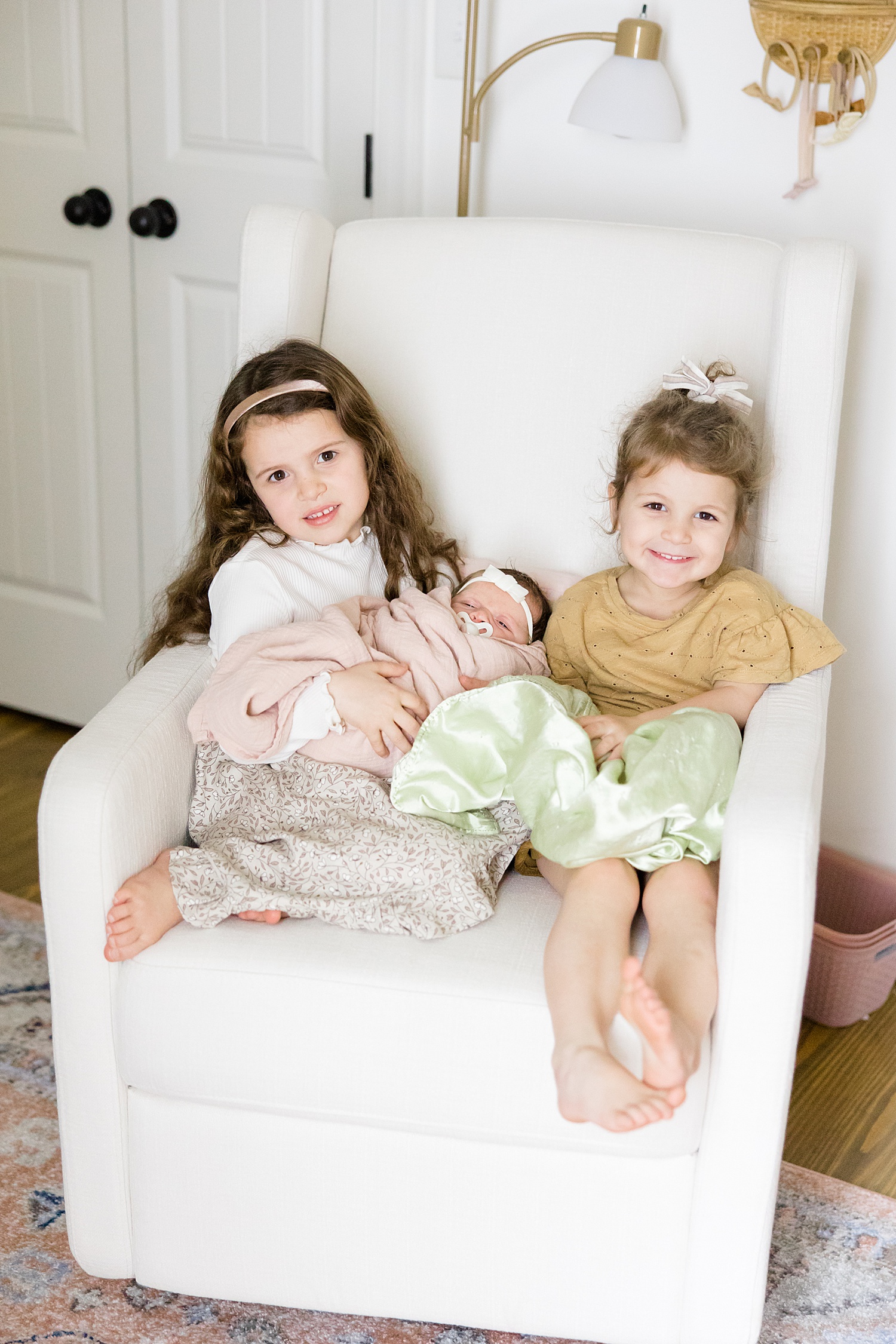 two sisters sit in chair holding baby sister