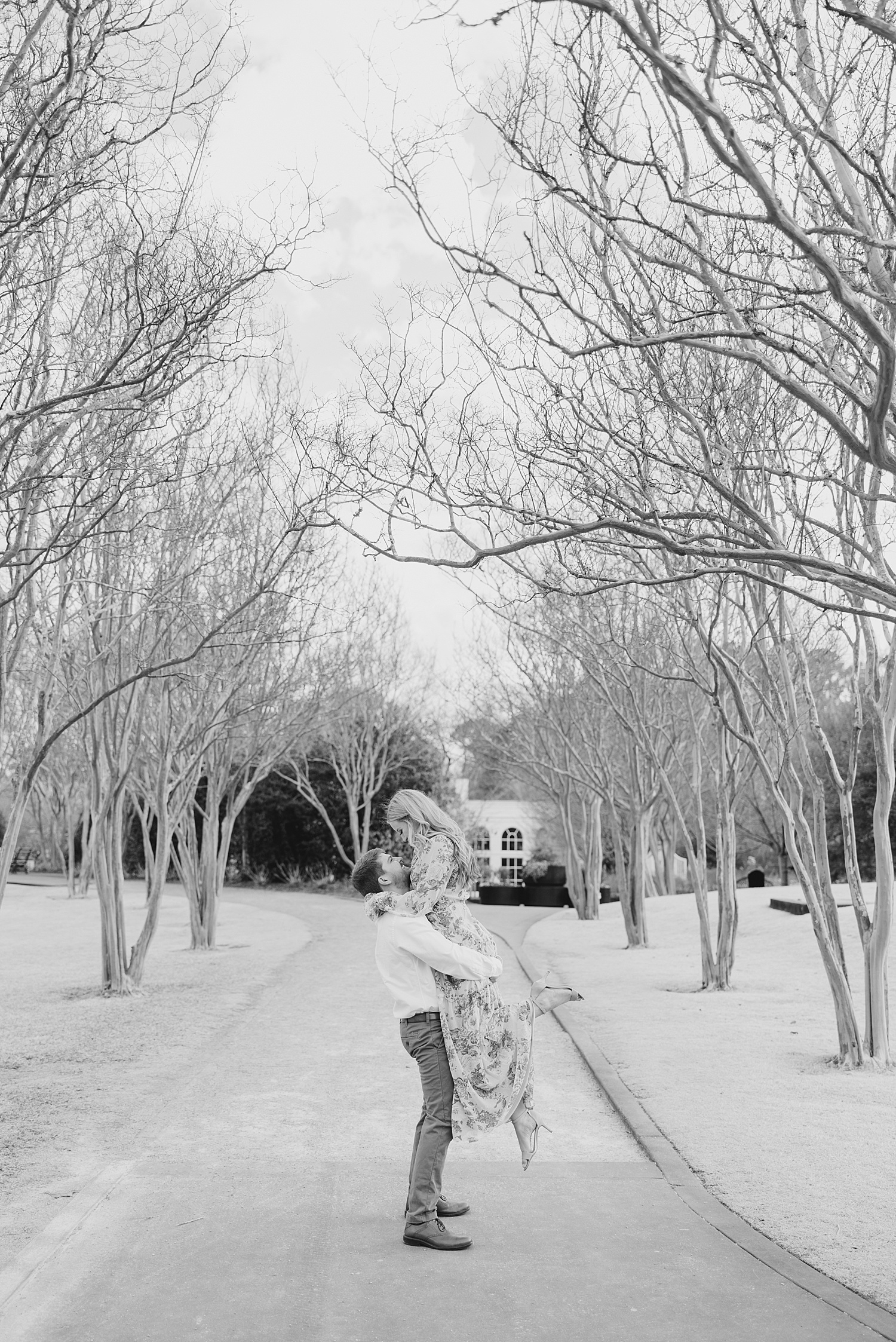 engaged couple kiss standing in tree lined driveway