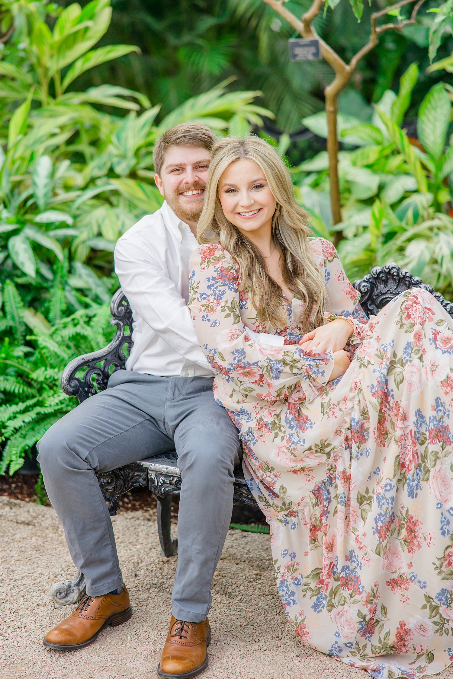 couple sit on bench in gardens during Downtown Birmingham Engagement Portraits