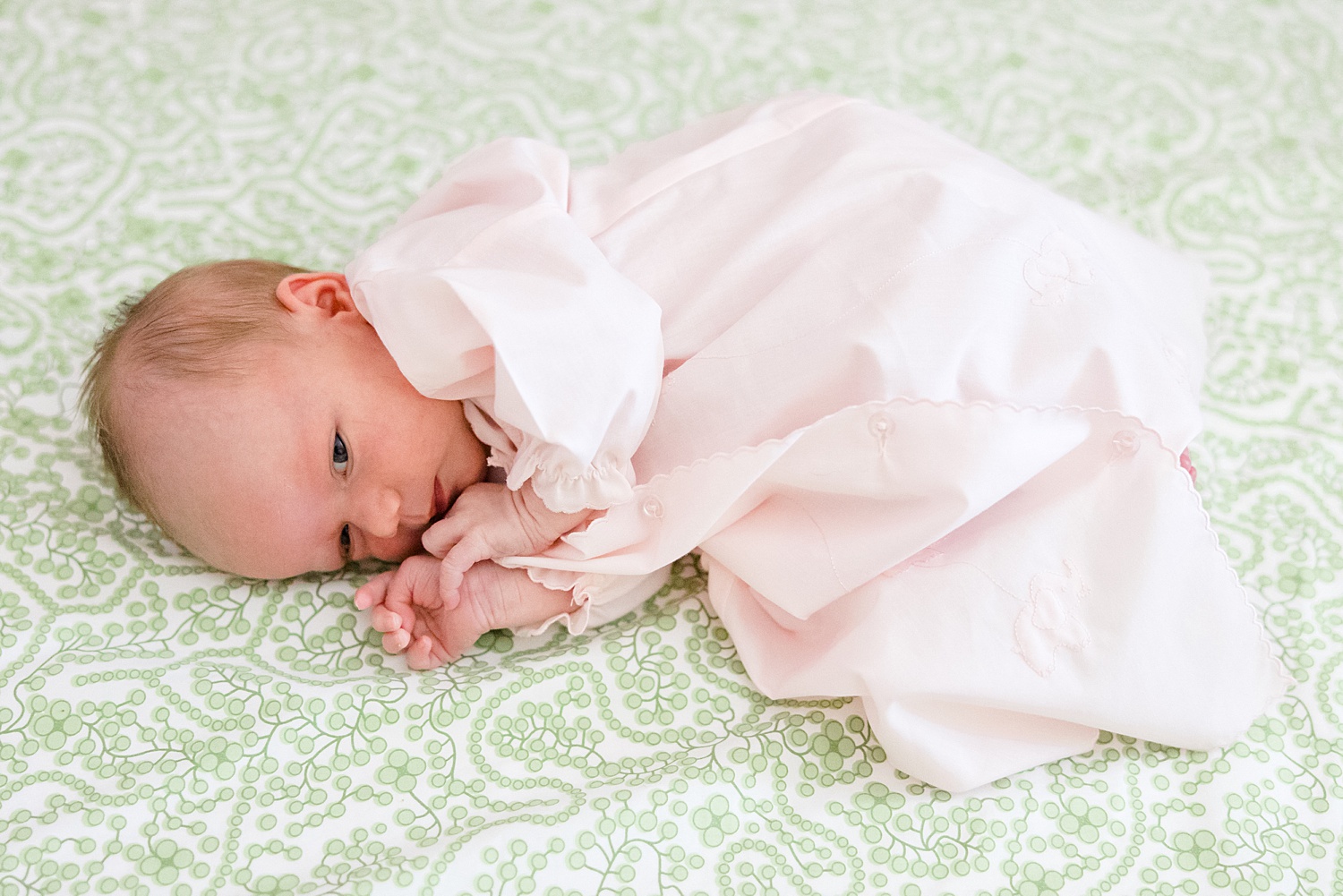 newborn lays on green patterned sheet