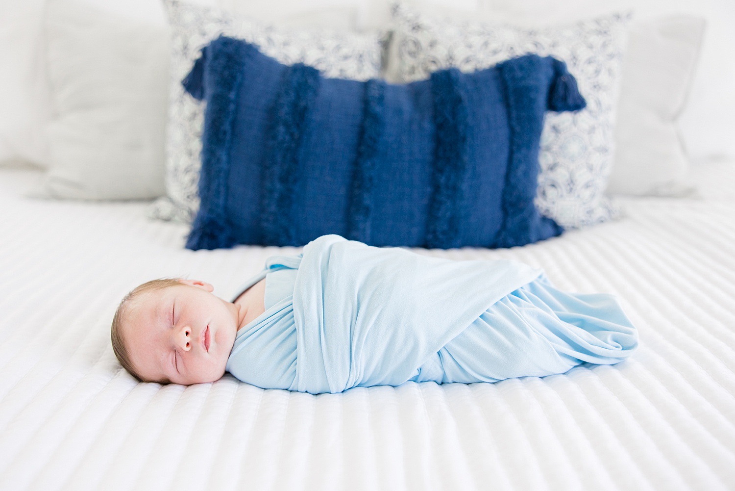 baby boy lays on bed swaddled in blanket