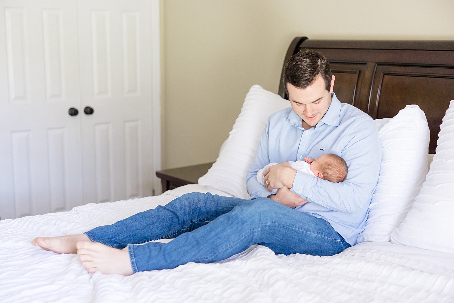 dad and newborn son sit on bed