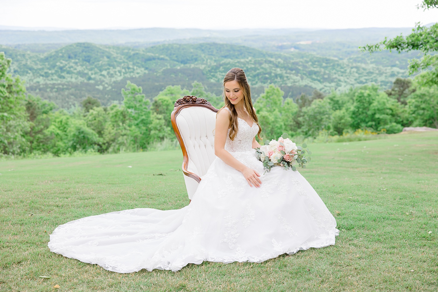 bride sits in white chair on top of a hill overlooking valley below 