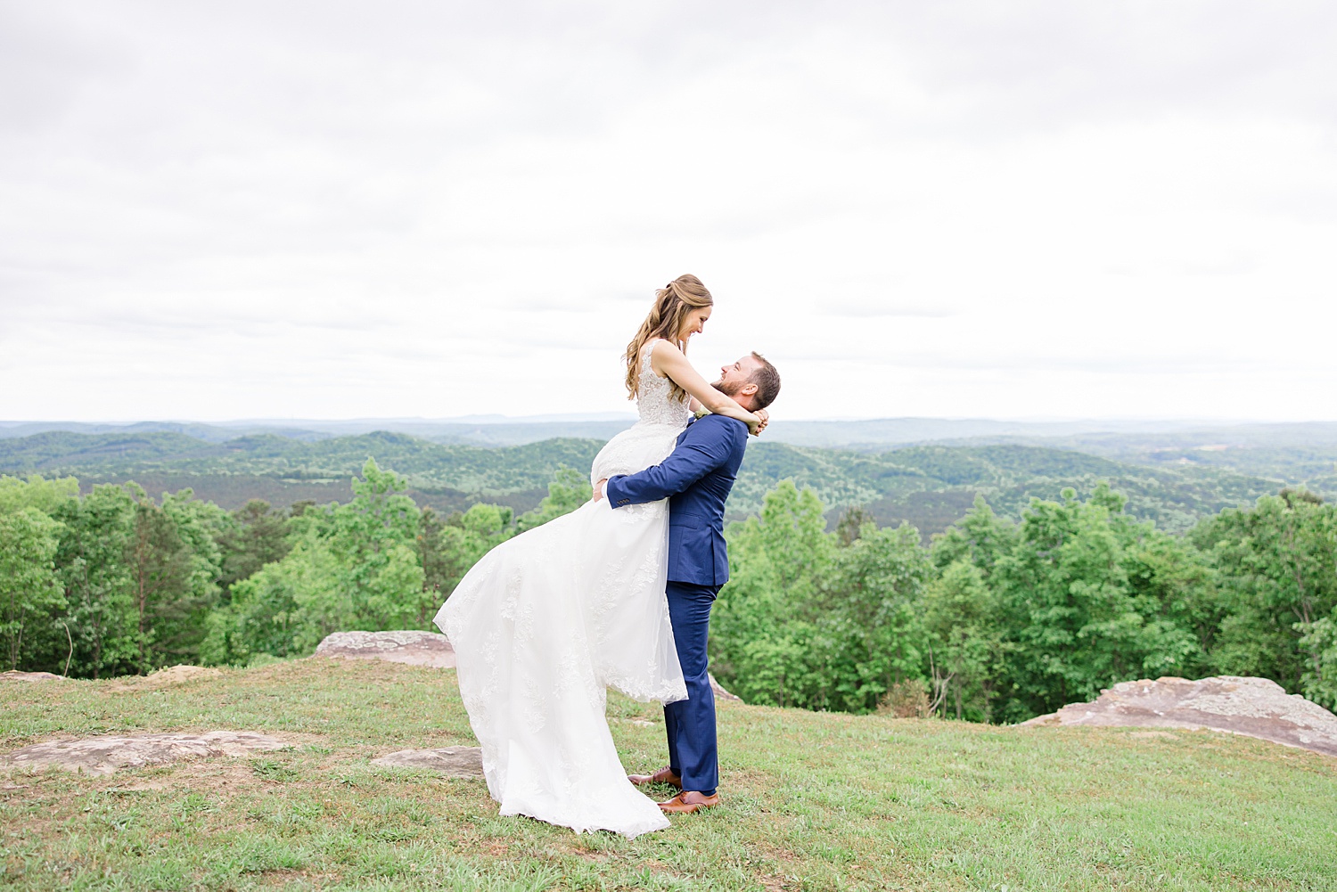 groom lifts his bride up standing on top of a hill