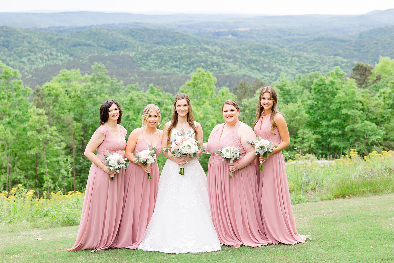bride with bridesmaids in blush pink dresses on hilltop 