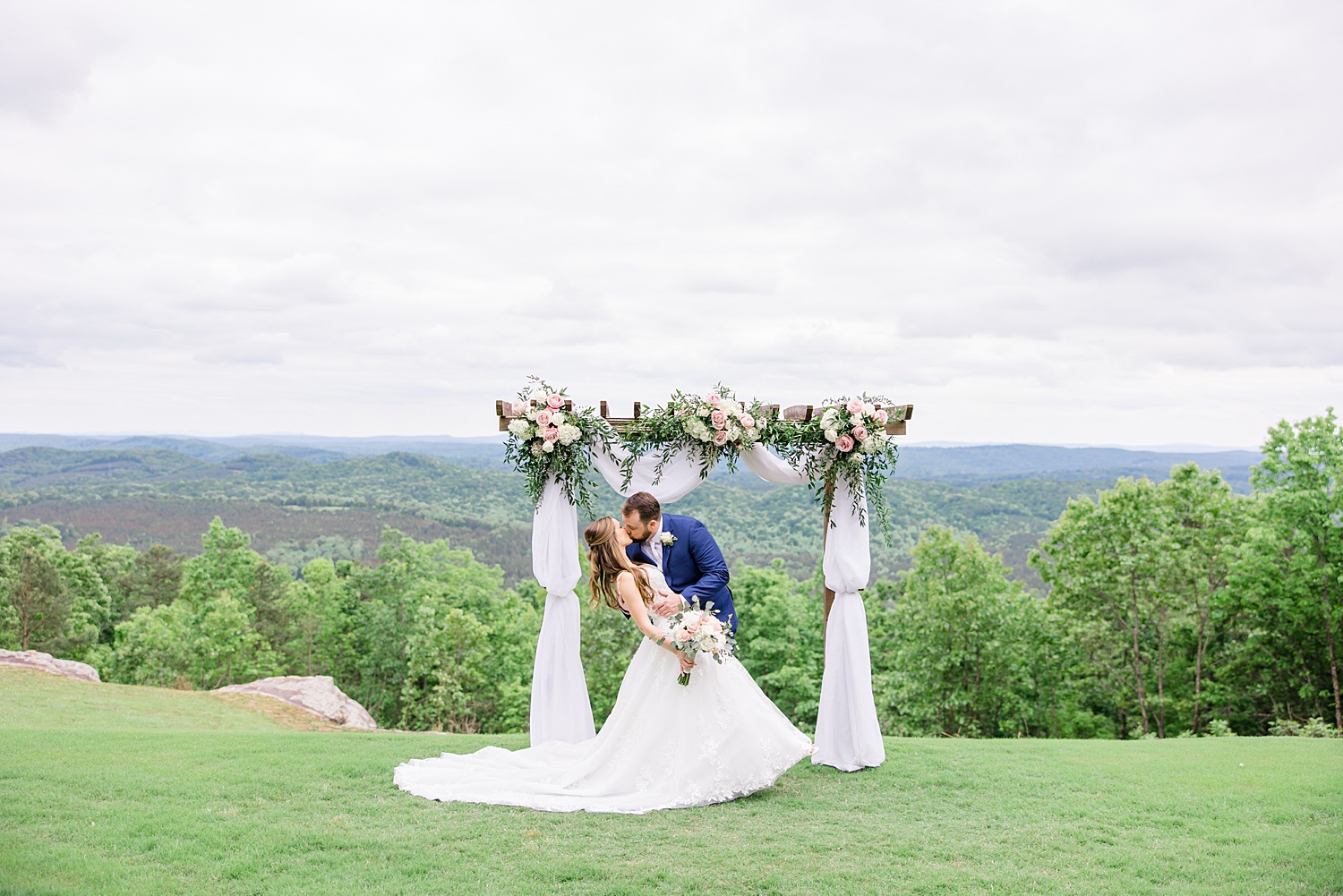 groom dips his bride and kisses her on hilltop before outdoor AL wedding ceremony
