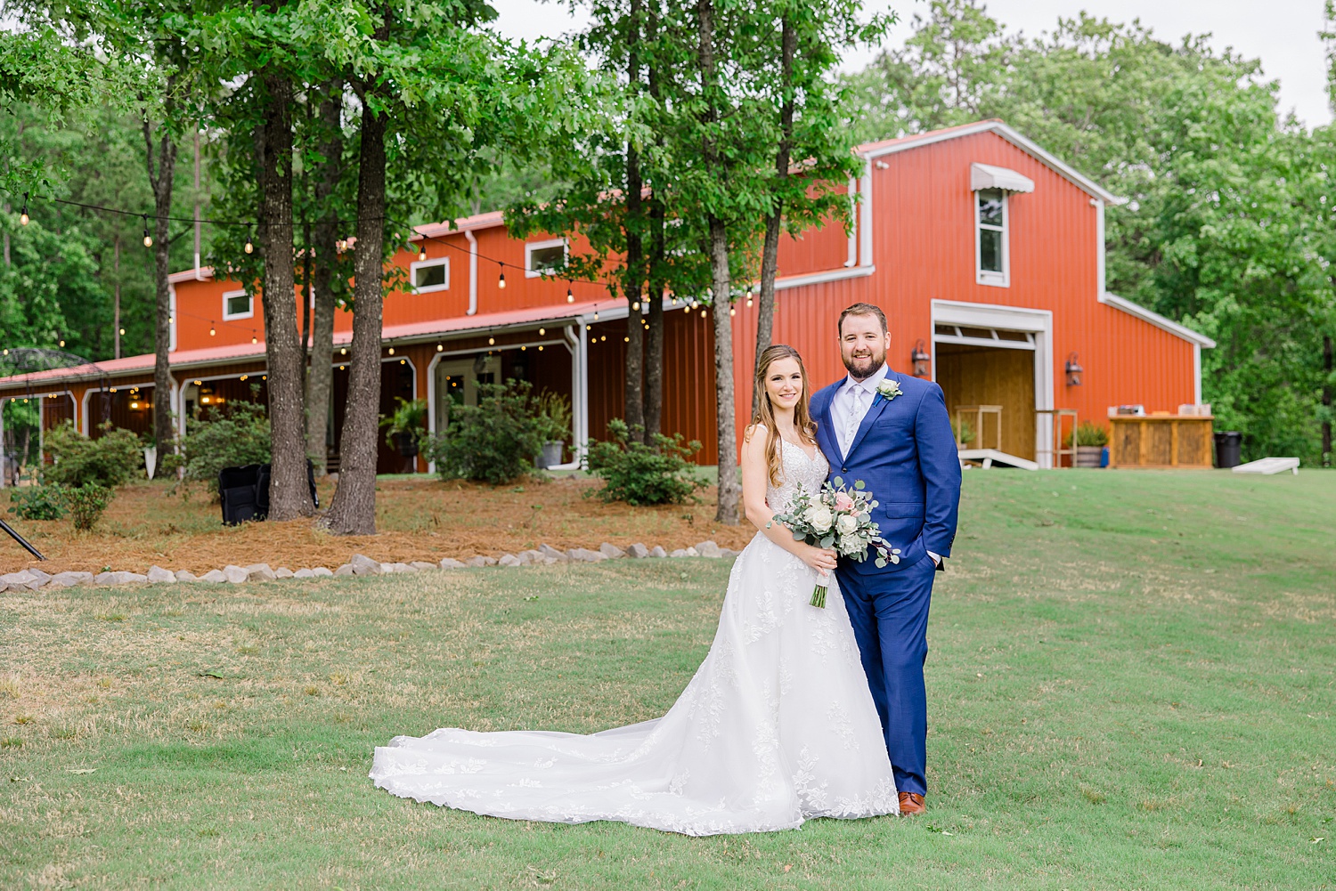 bride and groom stand in front red barn at Weddings at Cabin Bluff in Springville AL