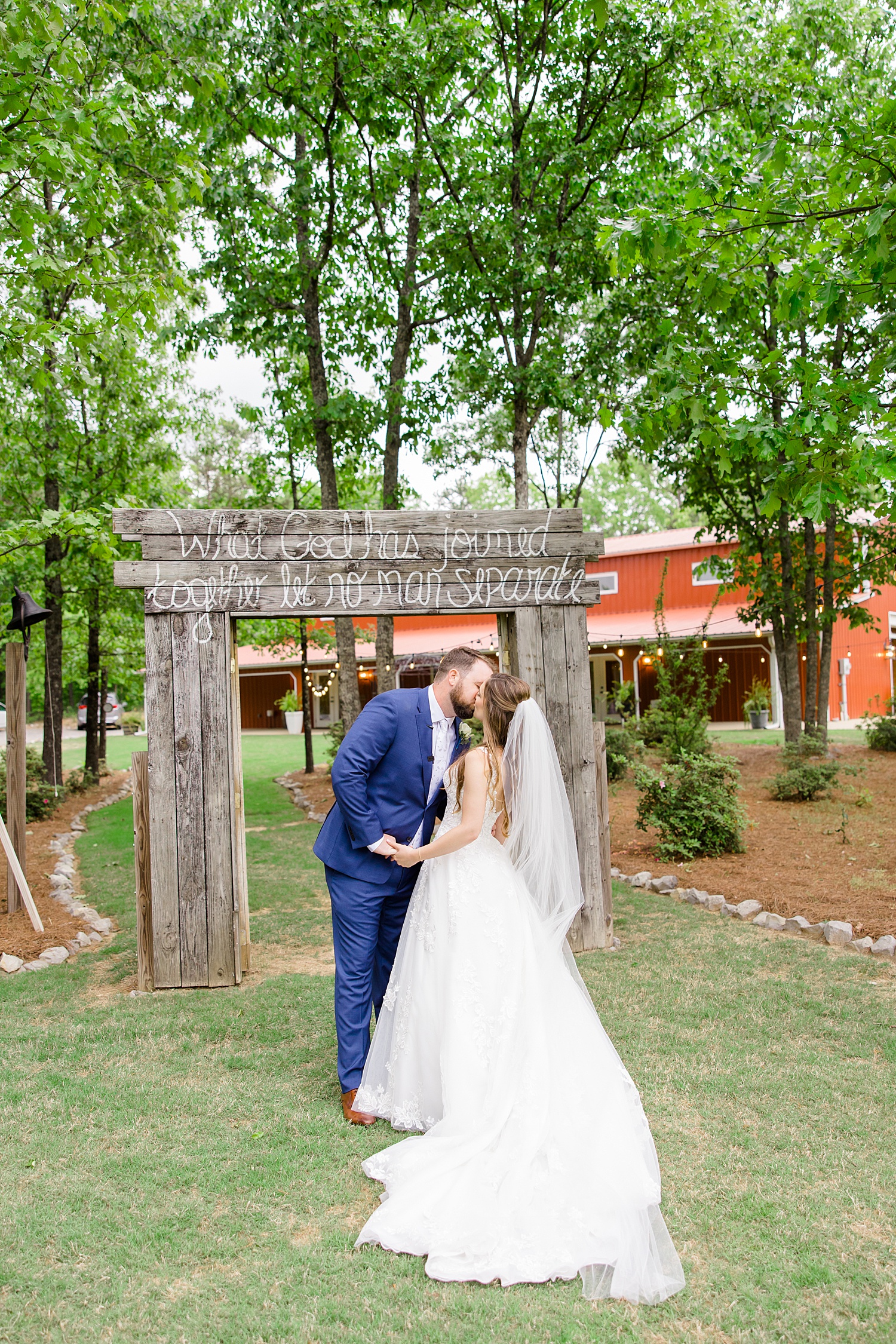 bride and groom kiss under wooden arch with quote on it after Romantic Spring Wedding at Weddings at Cabin Bluff