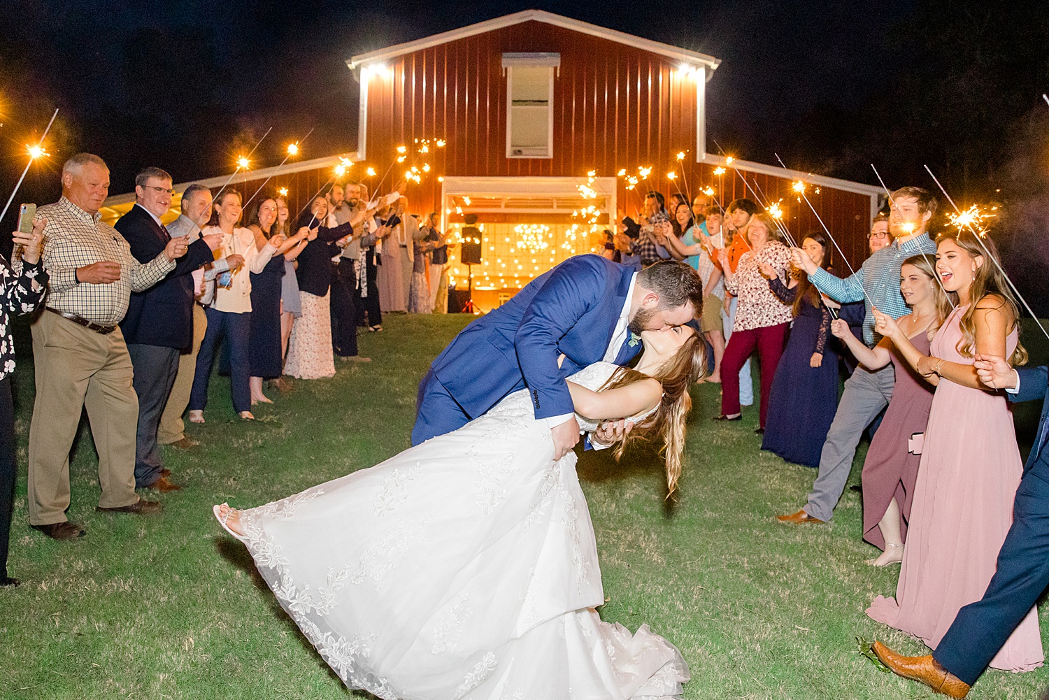 wedding guests hold sparklers as bride and groom exit reception and kiss