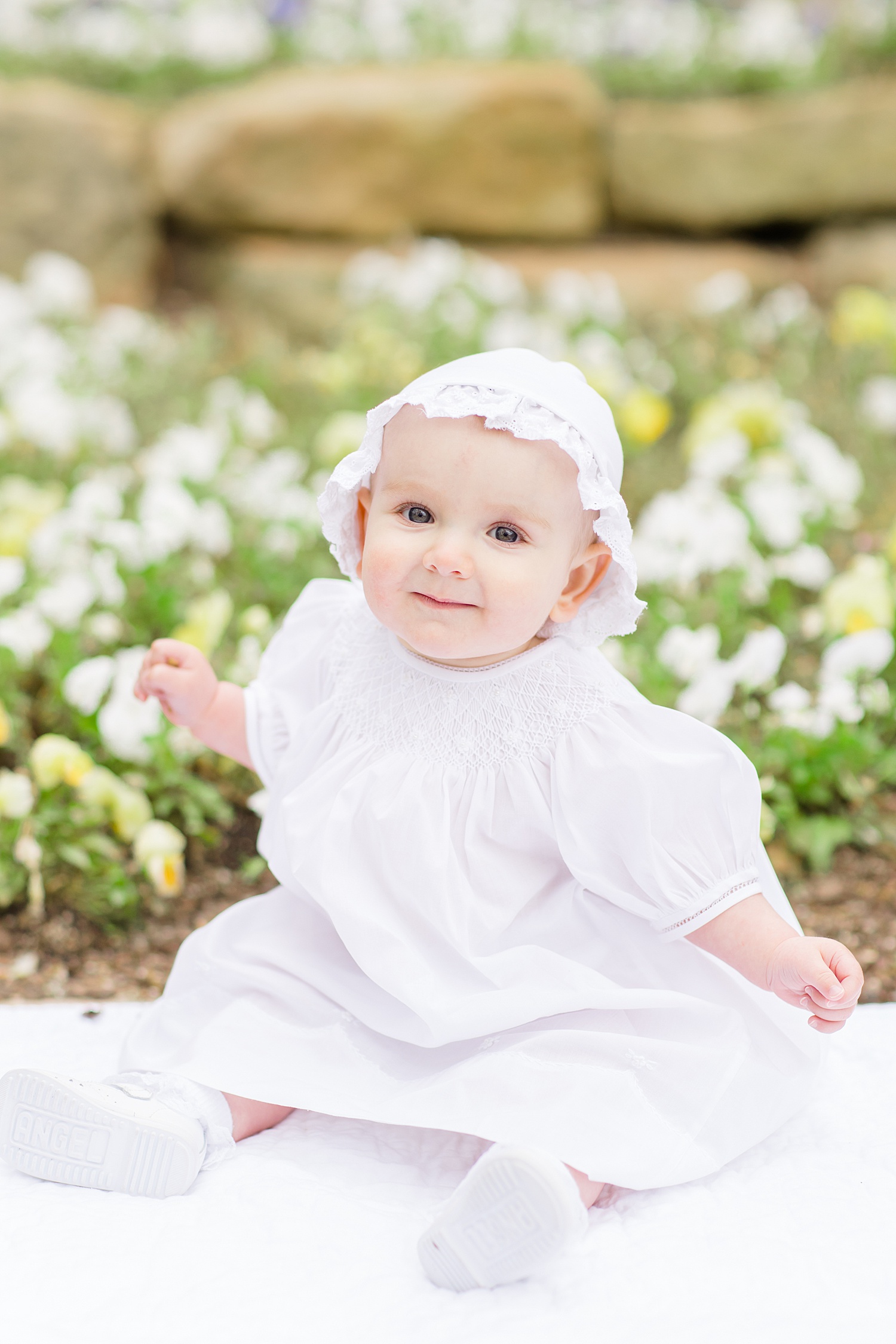 baby girl in white dress and hat sits for milestone portraits 
