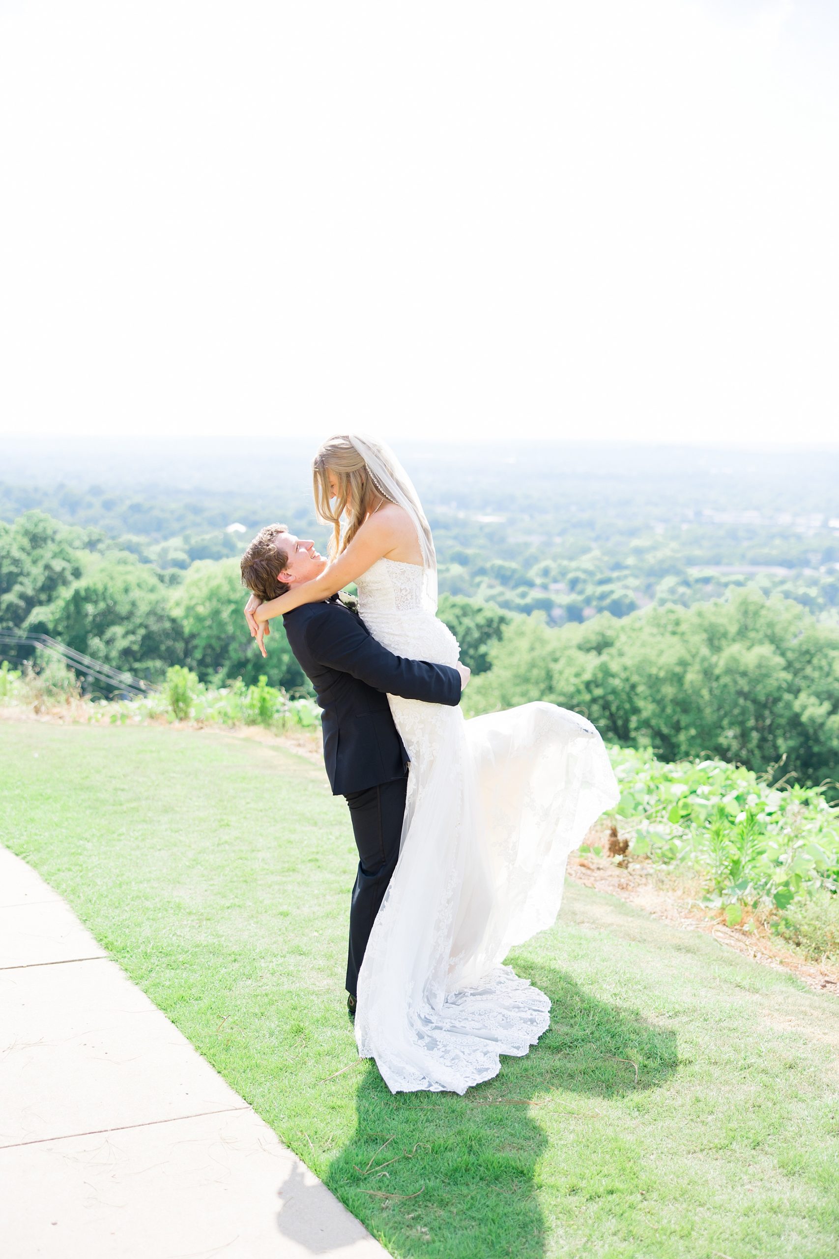husband lifts up his bride on hillside with amazing view