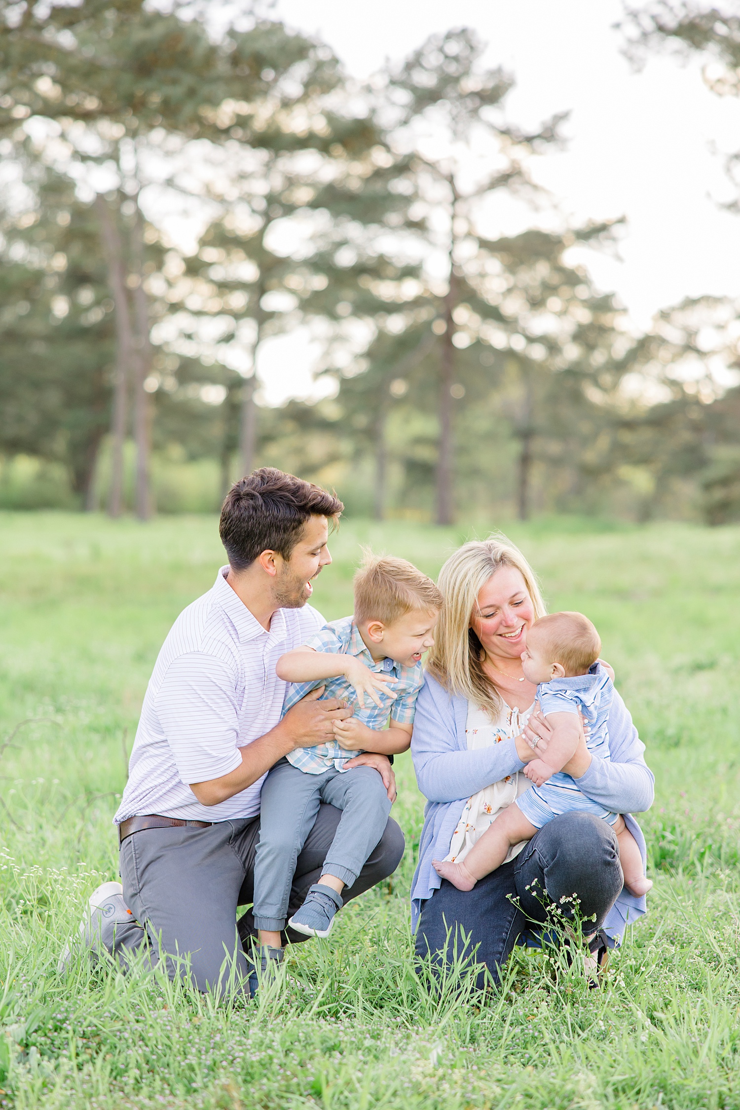parents sit in the grass with their two boys during Light and Airy Summer Family session