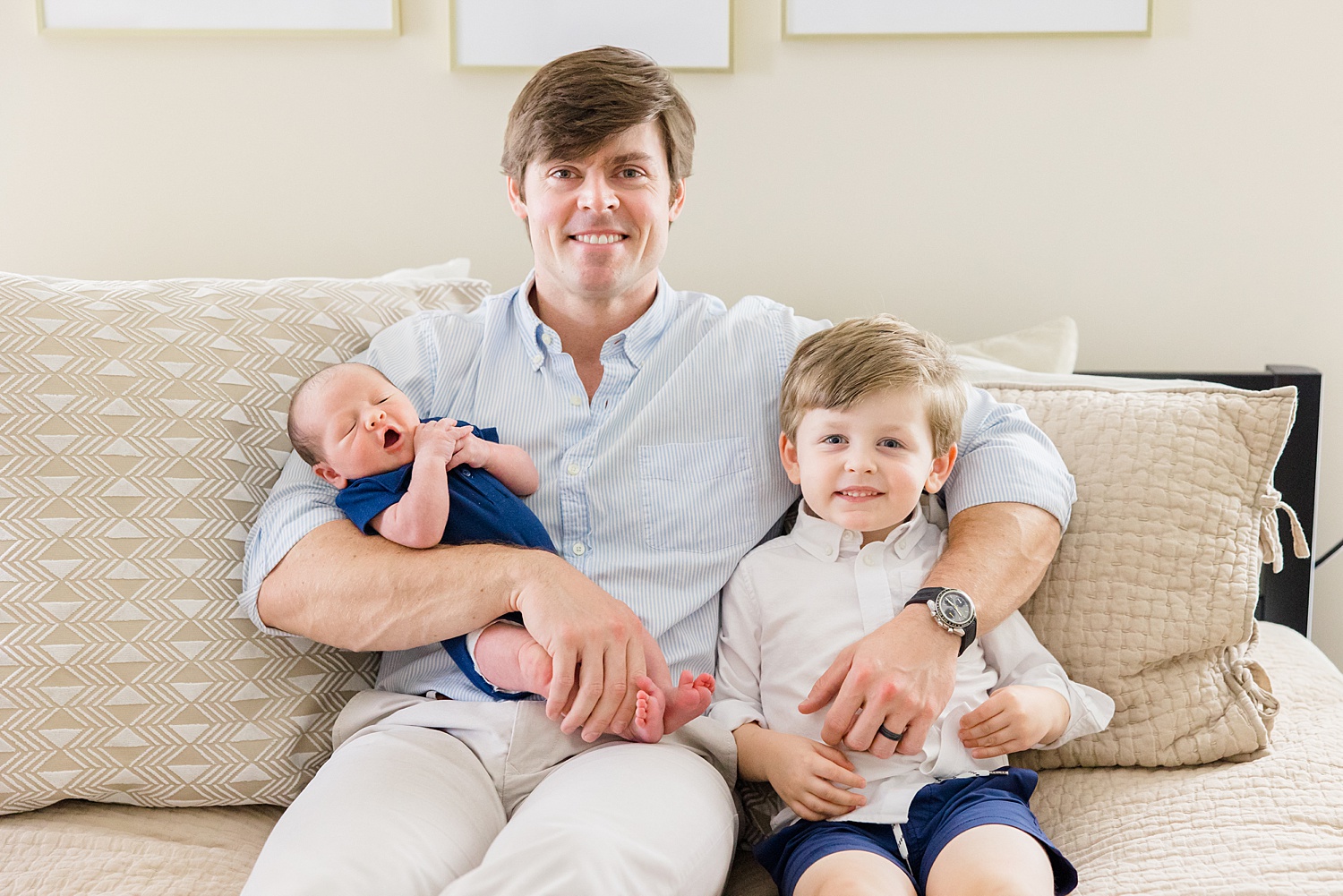 dad sits on couch with two sons during Cozy In-Home Newborn Session