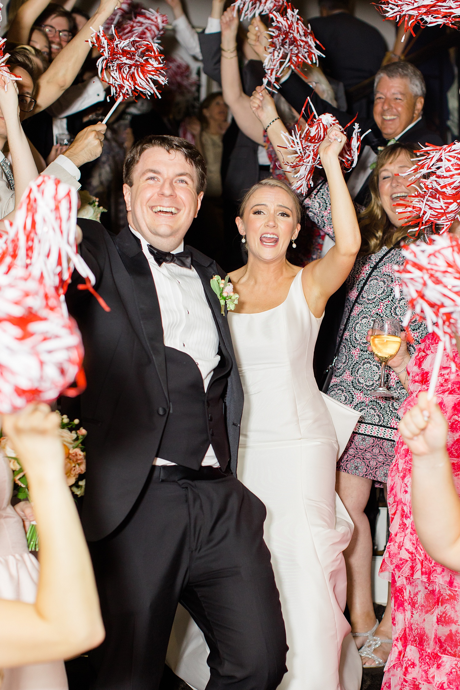 newlyweds exit reception with guests waving red and white pom poms
