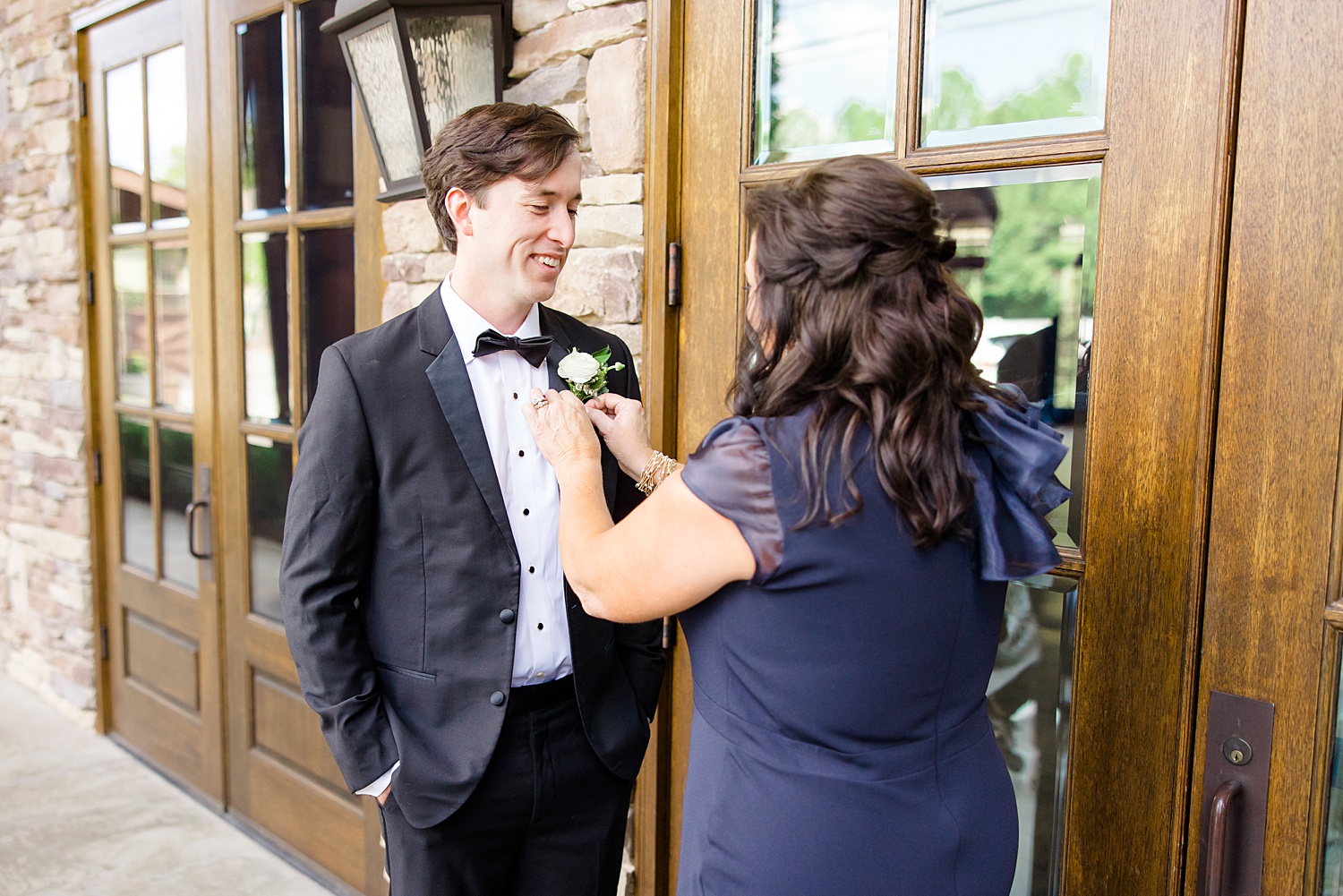 groom's mom helping him with boutonniere 