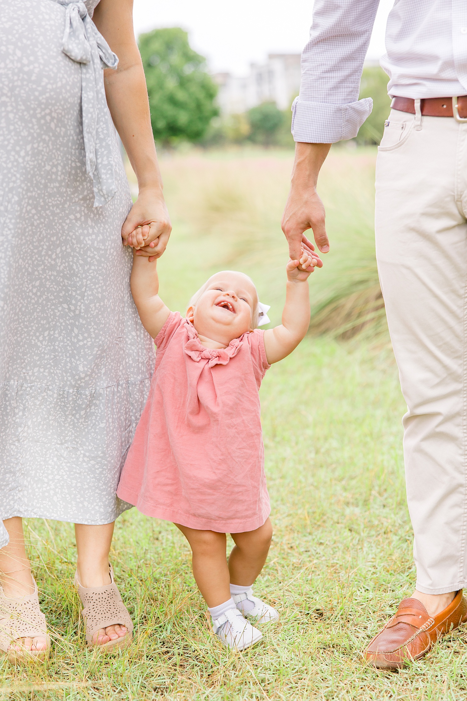 toddler girl laughs as she holds her parents hand during Railroad Park Family Session in Birmingham, AL