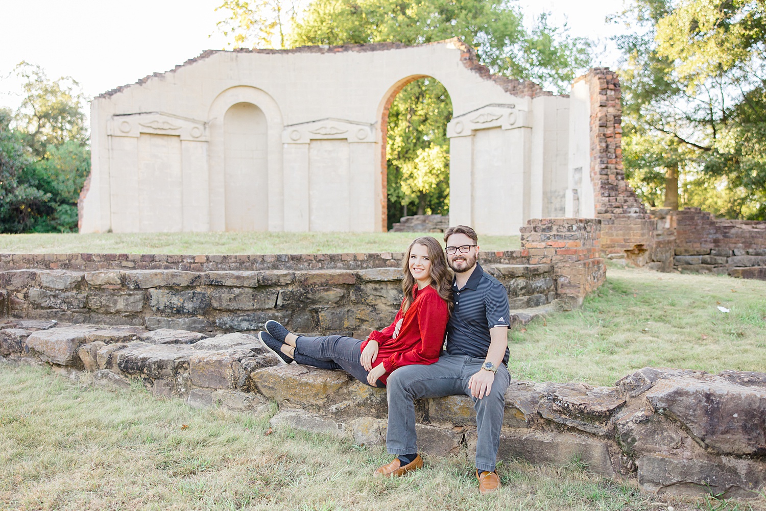 couple sit on stone wall in Capitol Park Engagement in Tuscaloosa, Alabama