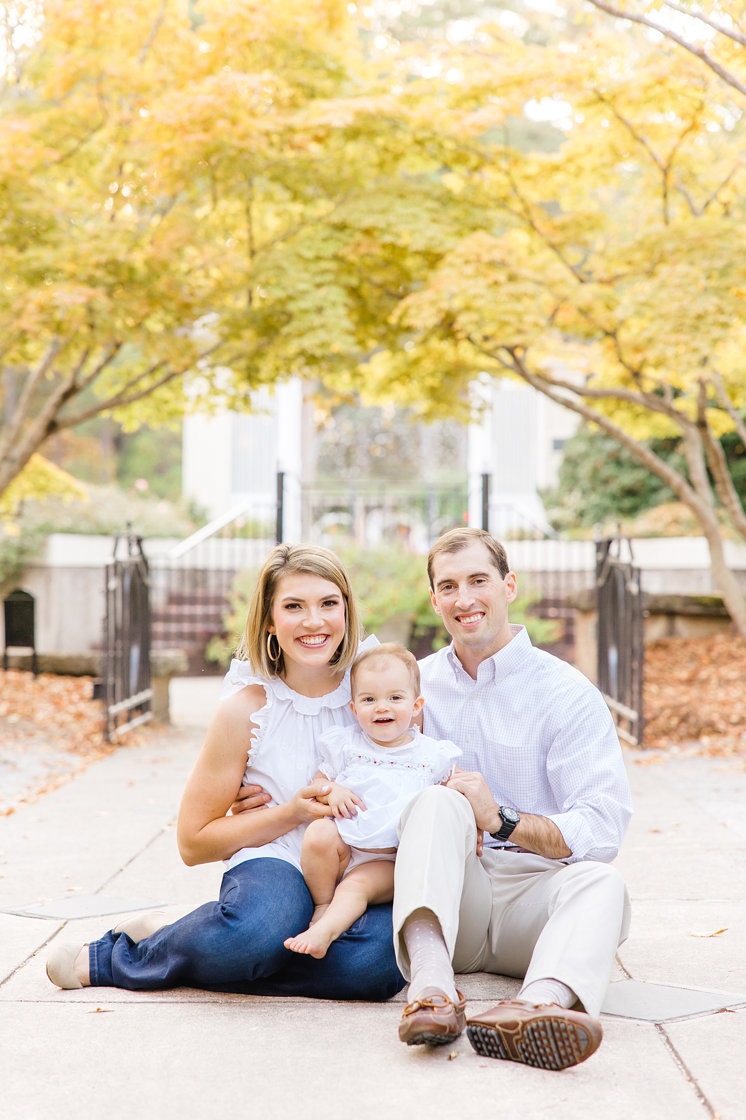 family of three sits on sidewalk during fall family portraits 