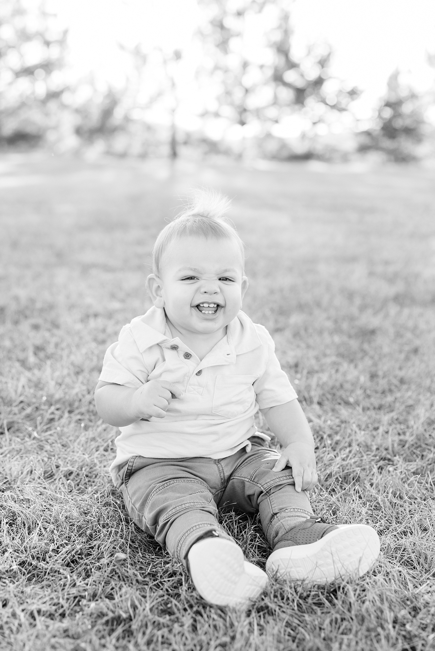 little boy sits in the grass and smiles