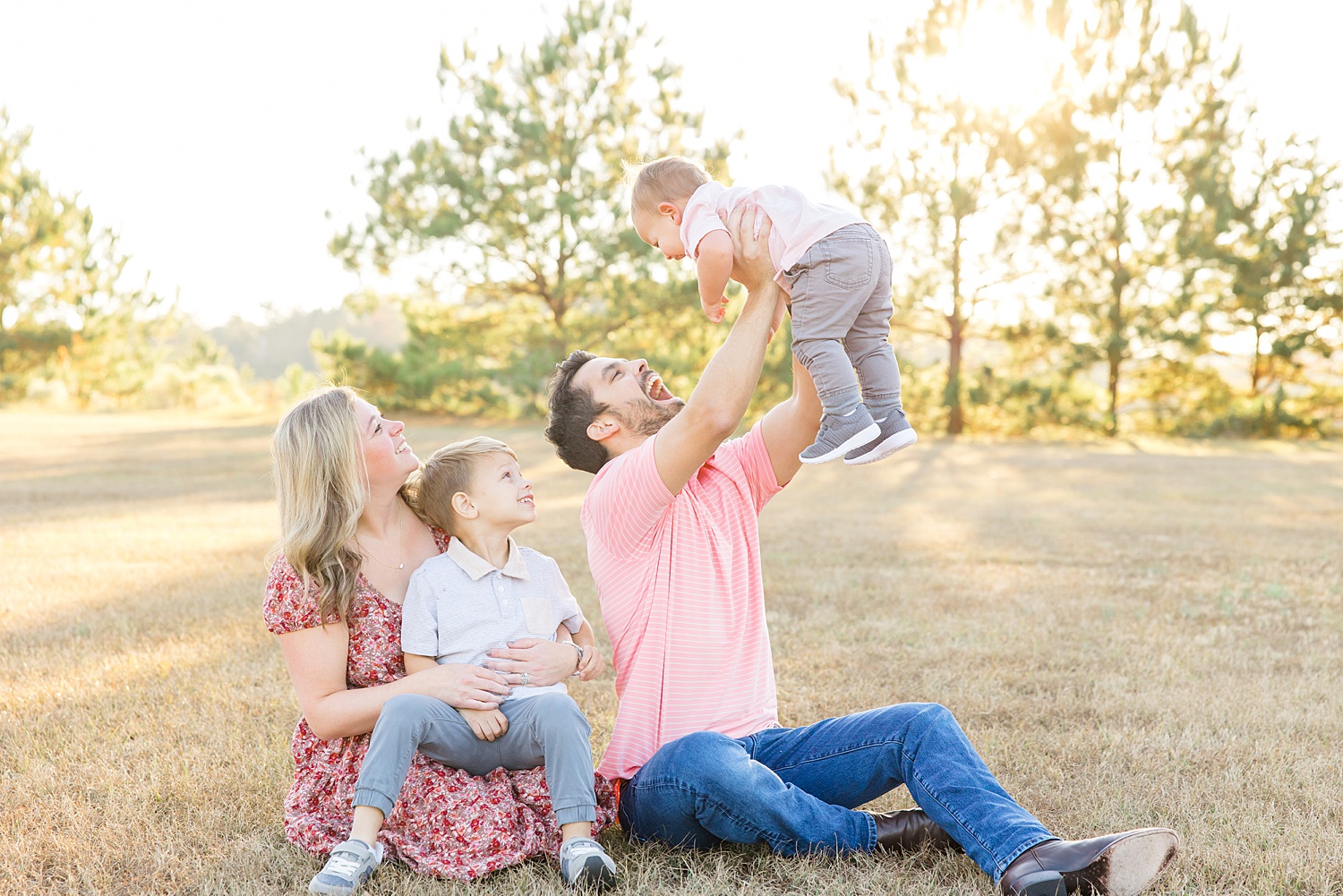 dad lifts his youngest son in the air as the family sits on the ground during family session