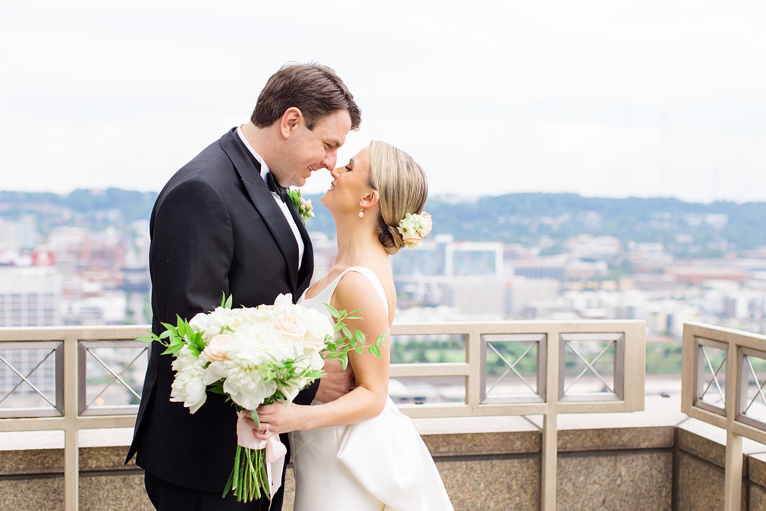 newlyweds kiss on balcony with downtown Birmingham skyline in the background