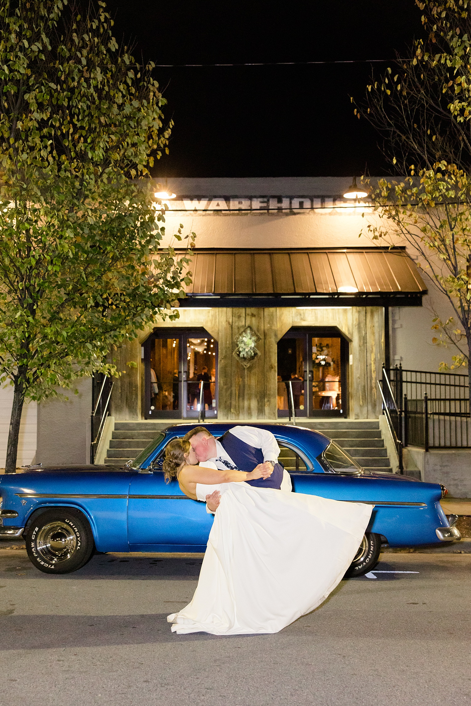bride and groom kiss in front of old car 