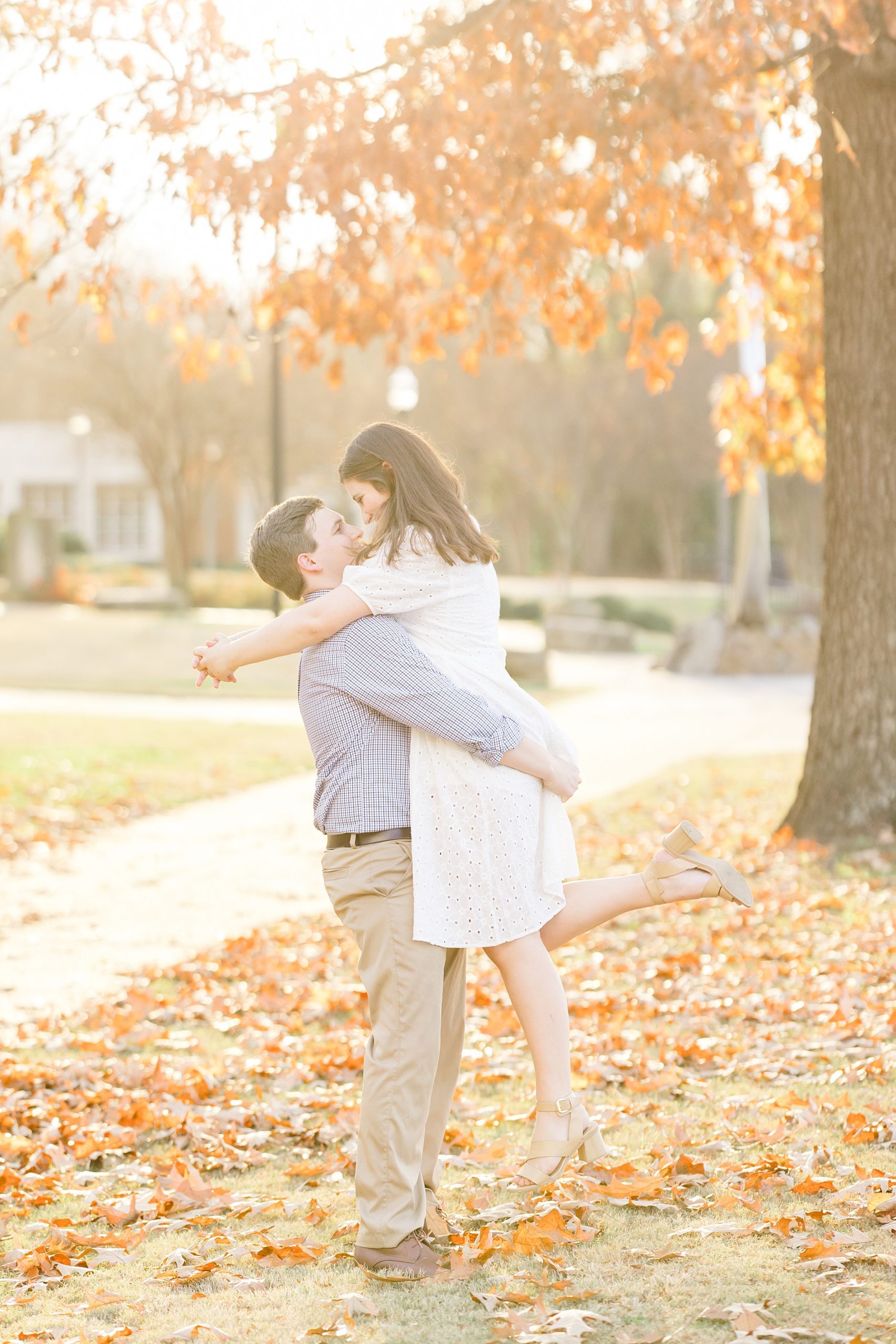 man lifts his fiance up in the fallen leaves