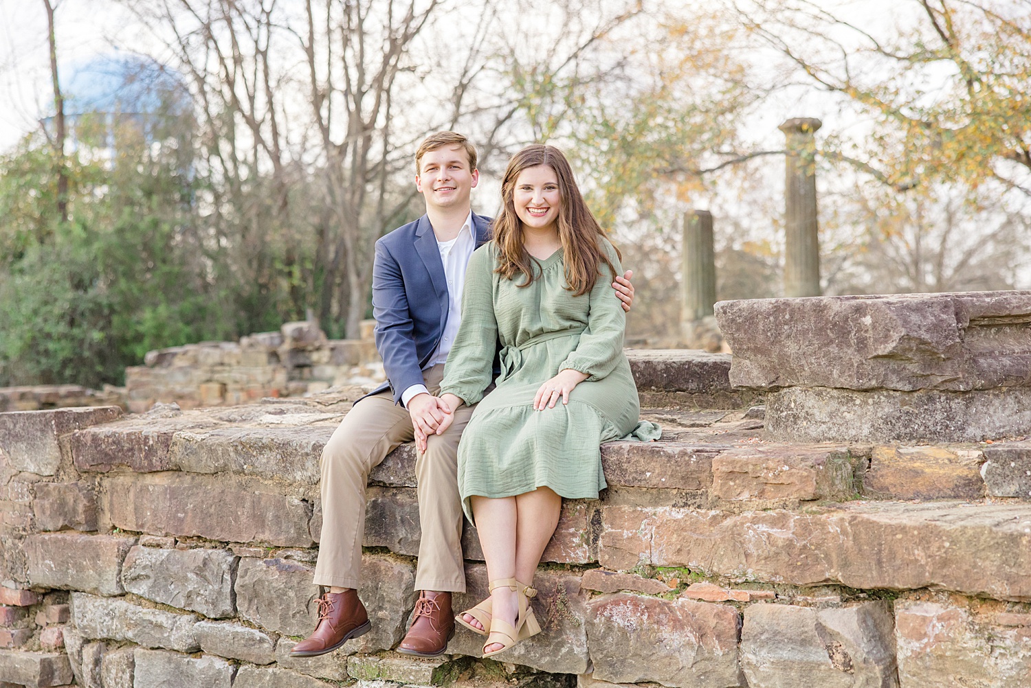 newly engaged couple sit on stone wall for engagement photos