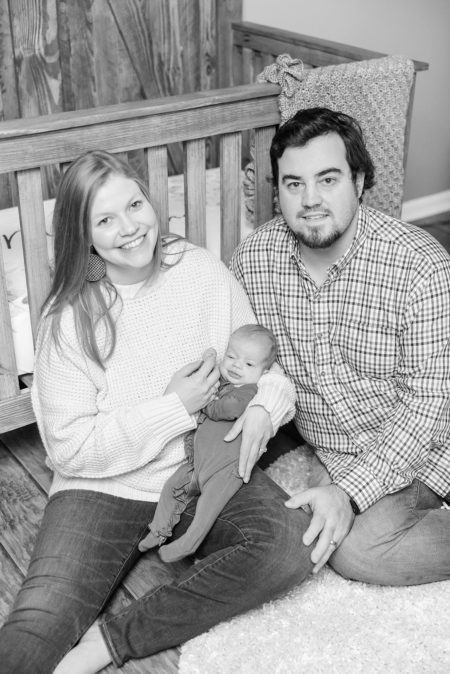 parents hold newborn sitting in front of crib