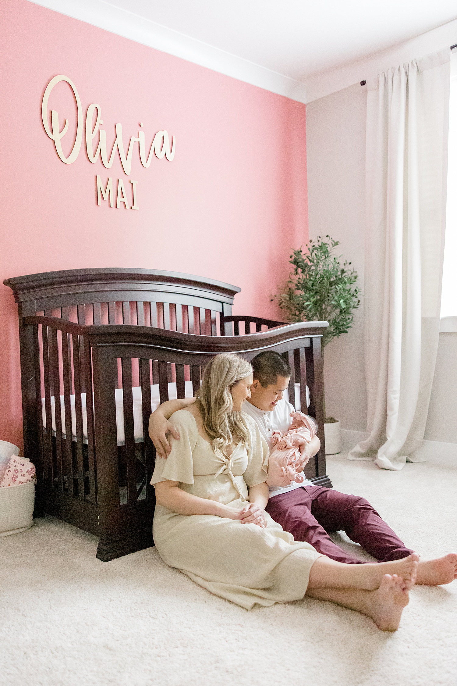 parents hold their baby girl sitting on the floor next to crib