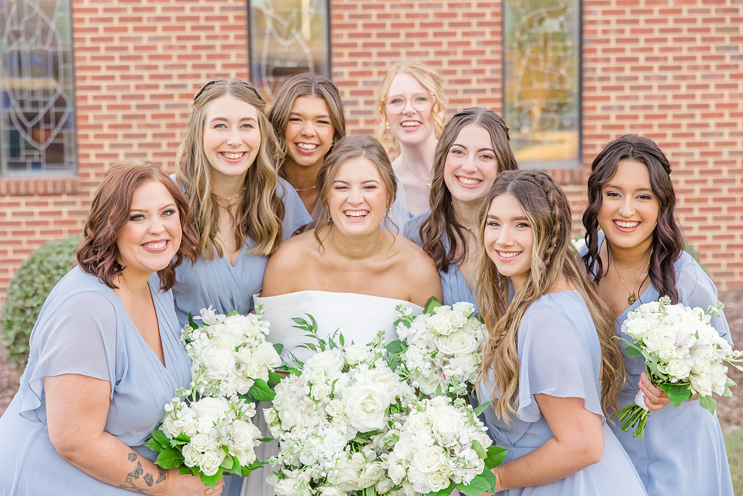 bridesmaids in dusty blue dresses with bride holding white bouquets  