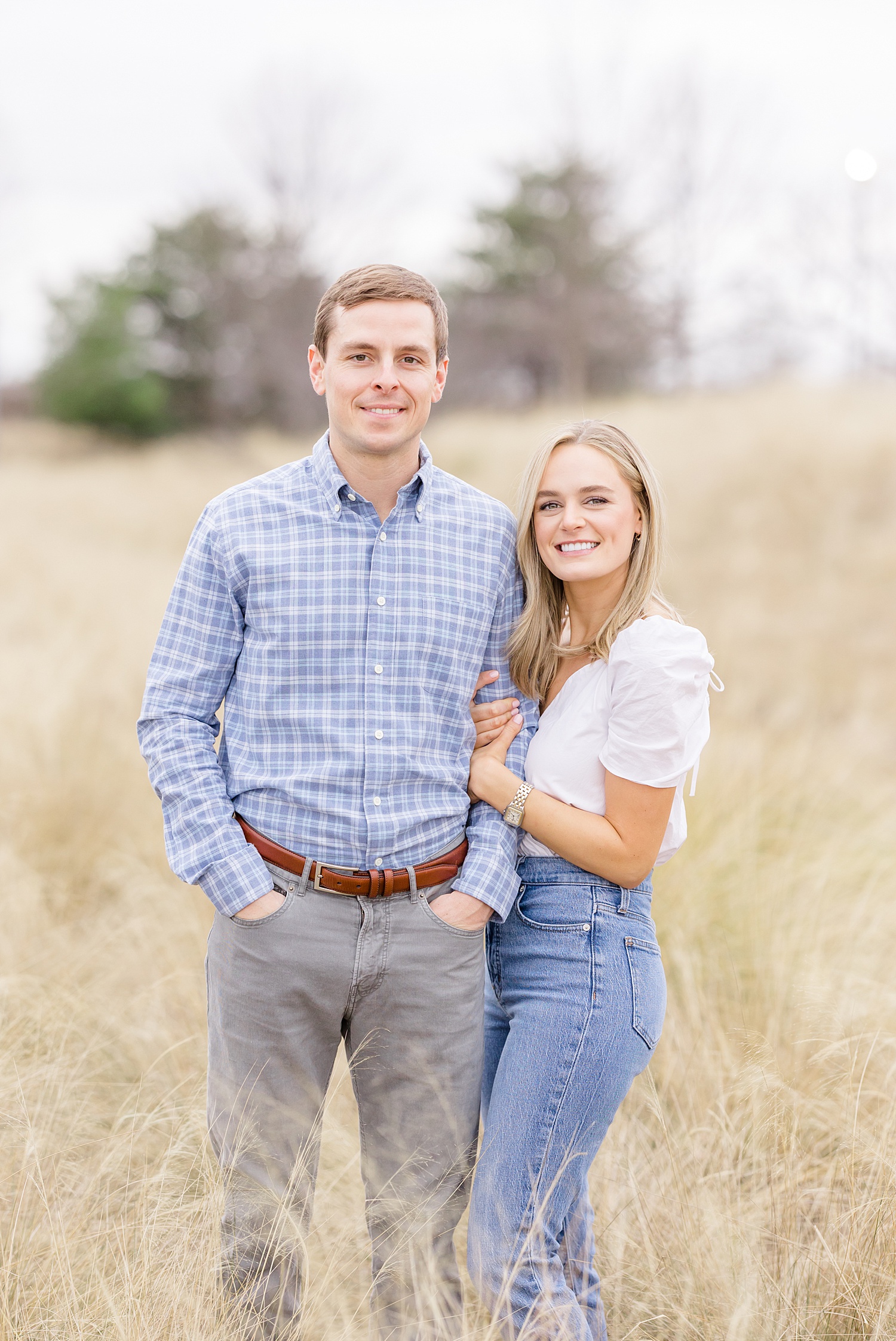 couple stand in field of tall grass for engagement portraits 