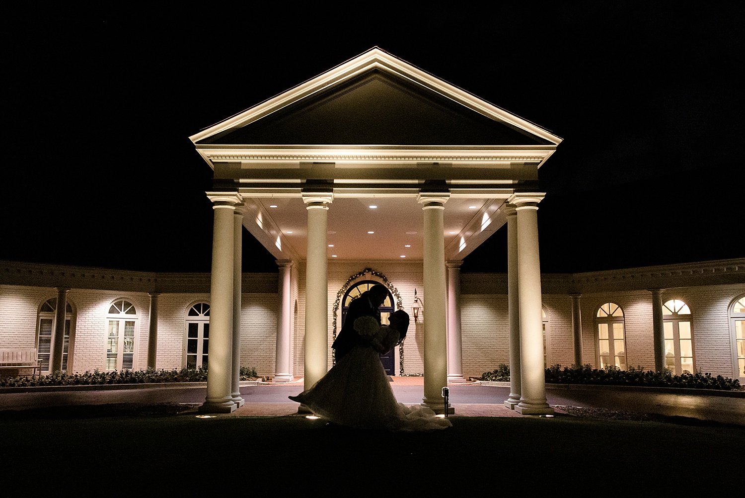 Romantic wedding venue lit up at night with the silhouette of the bride and groom 