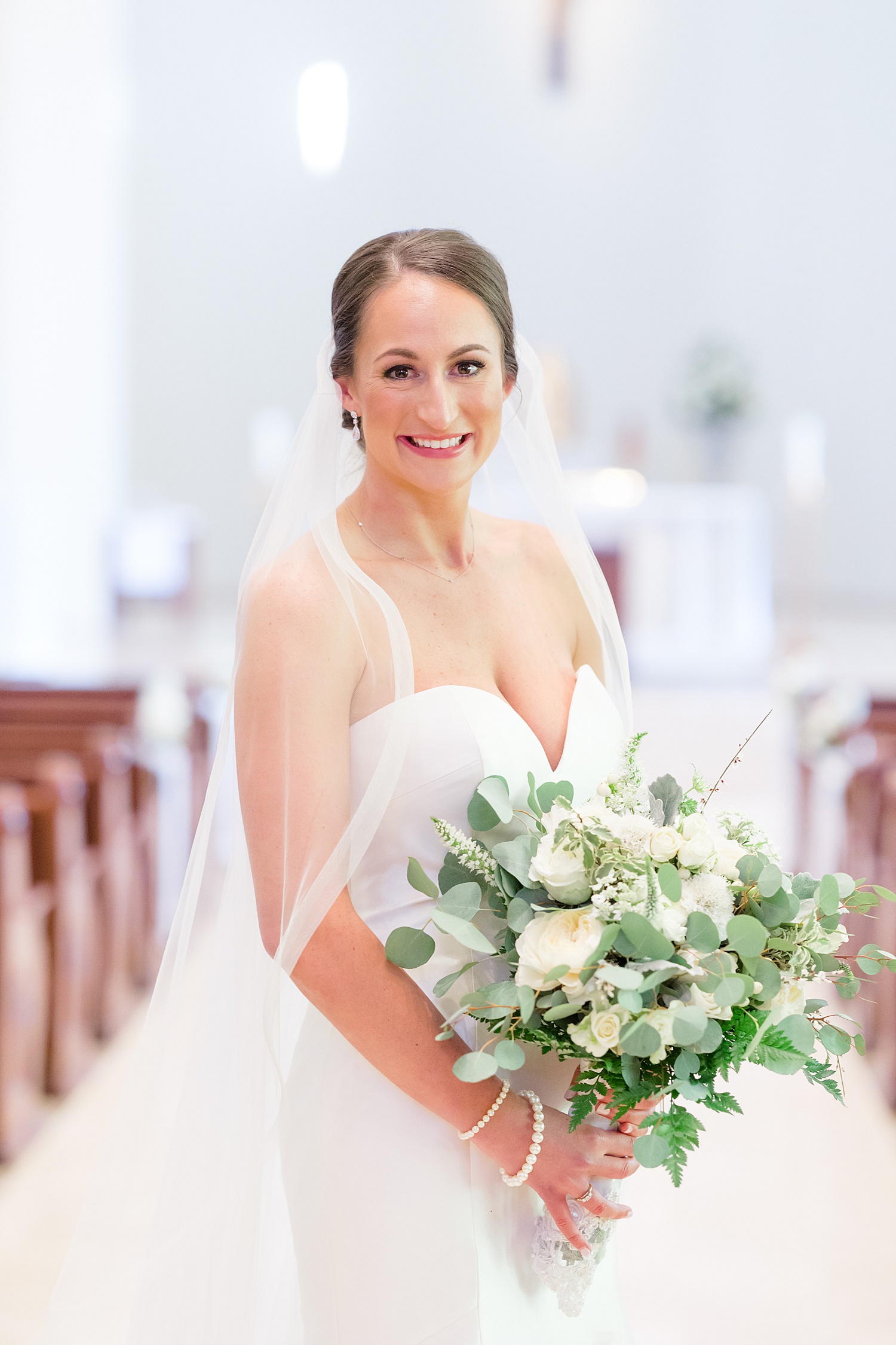 classic bridal portraits in church holding classic white bouquet with greenery