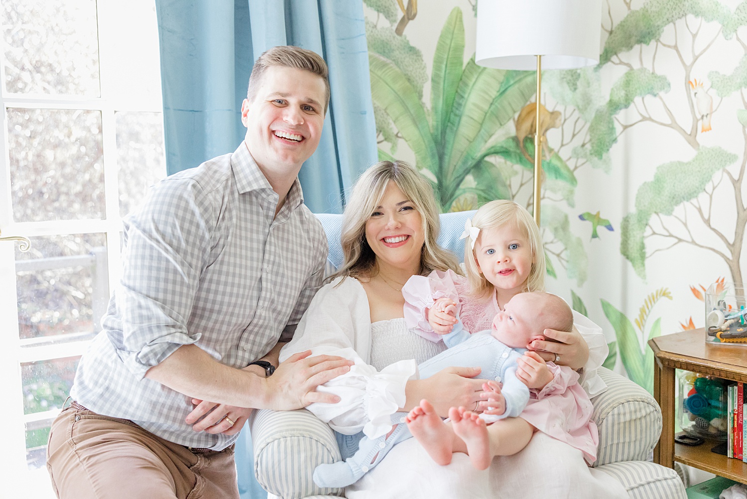 family of four sit together in newborn's nursery 
