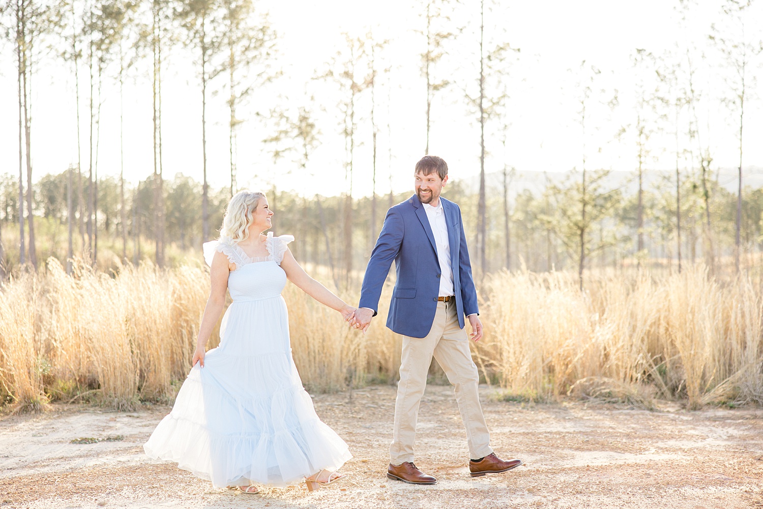 man leads his fiancé  as they walk by field of tall grass