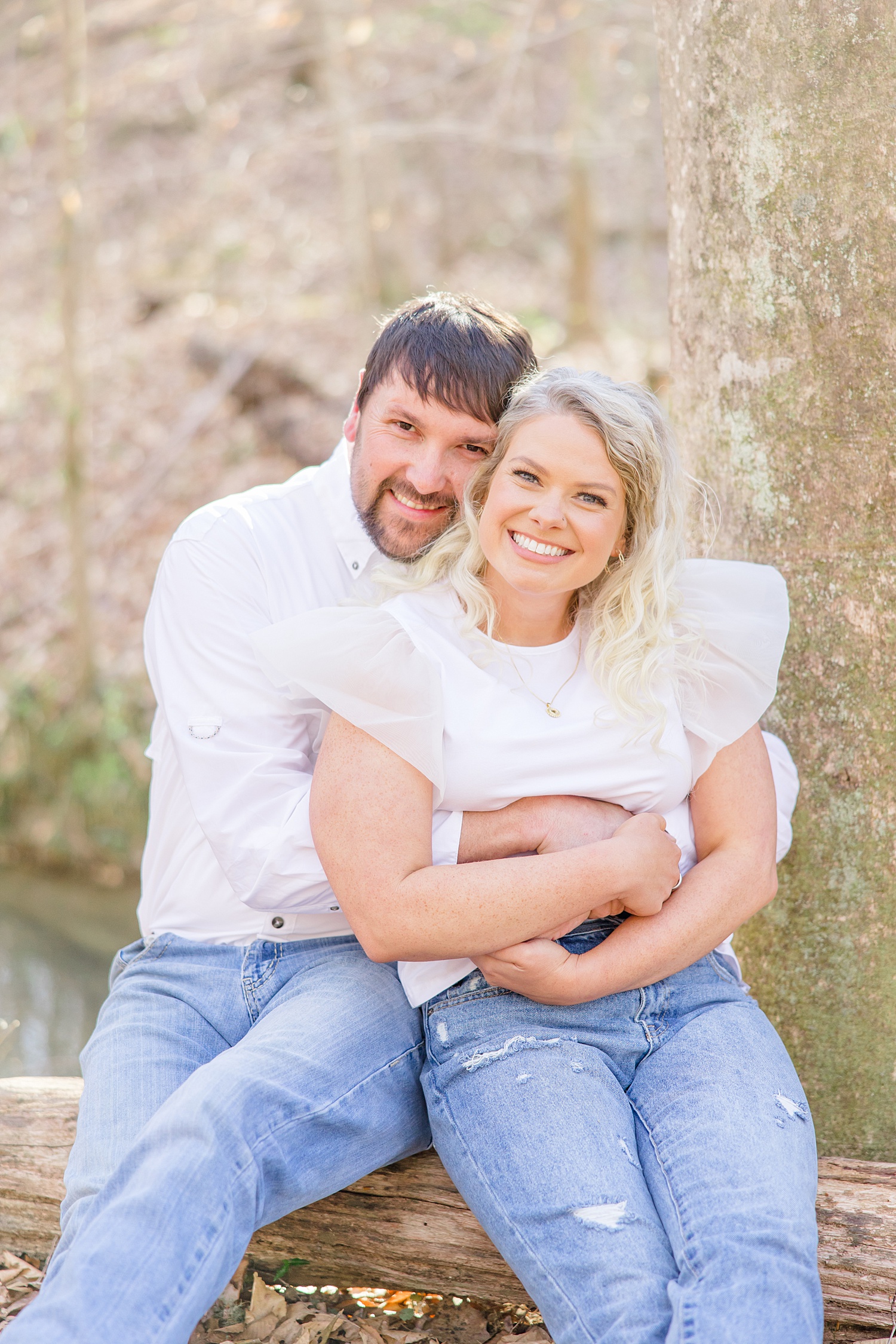 engaged couple sit on log in woods during their nature themed engagement session 