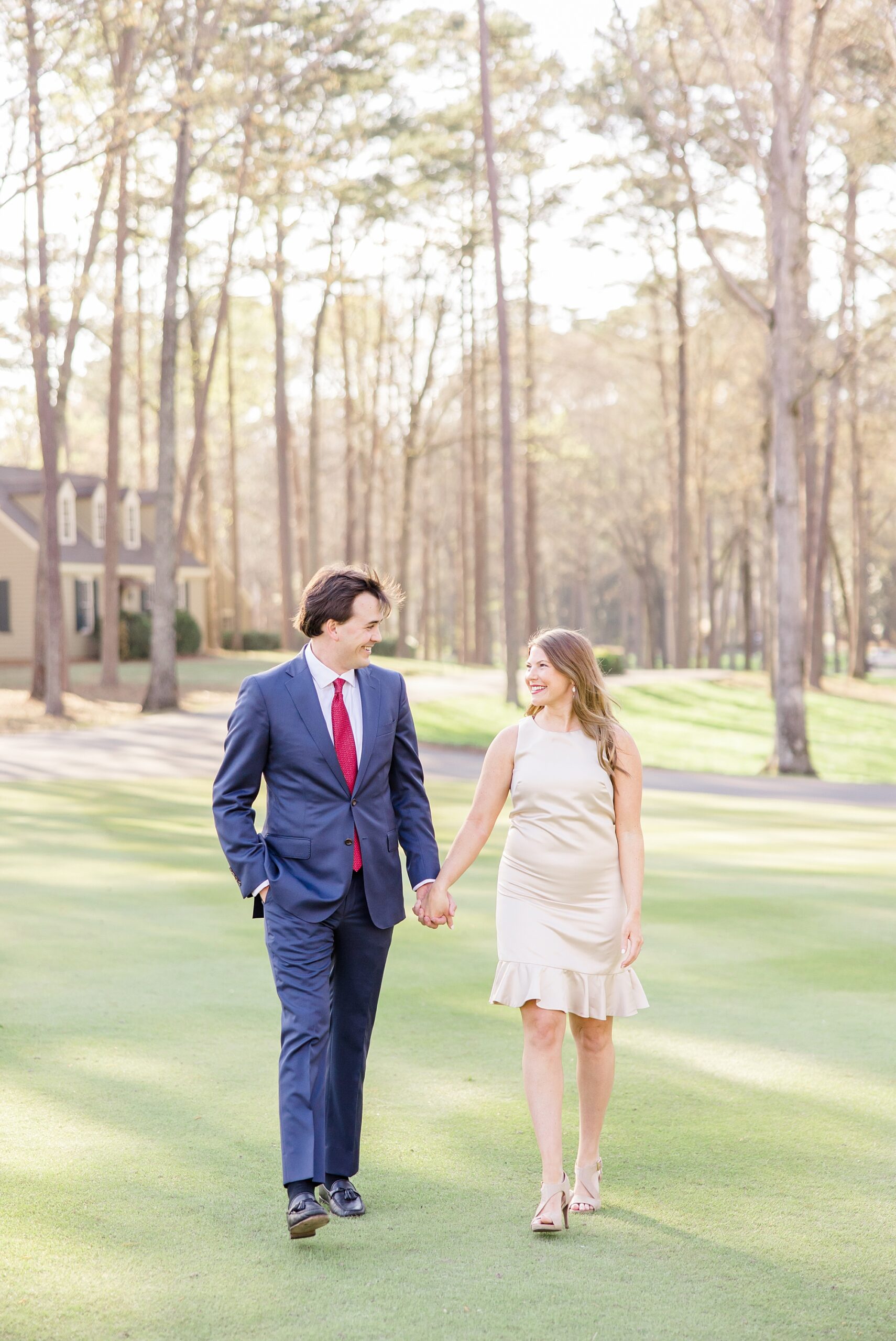 engaged couple walk together across the greens holding hands