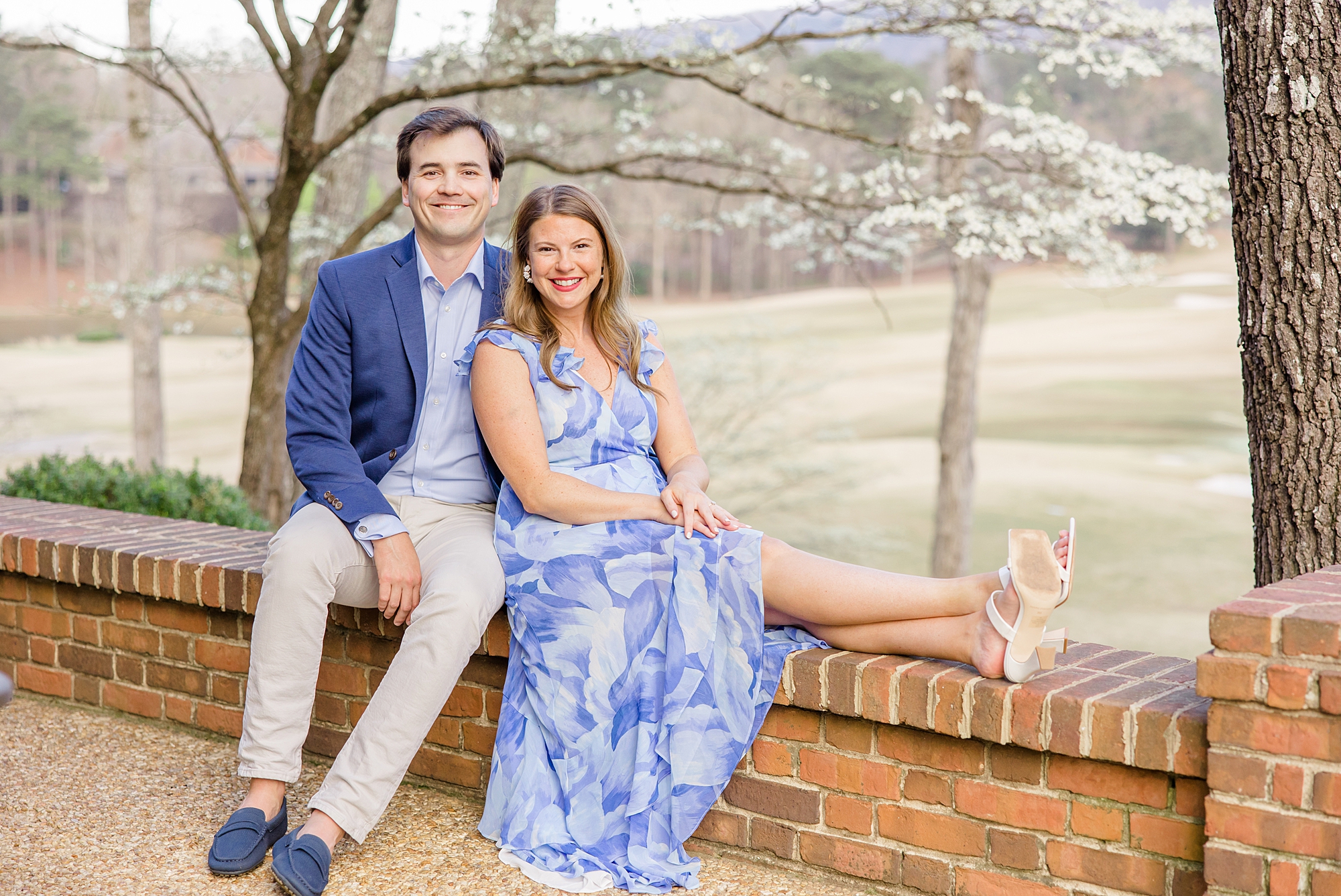 couple sit on brick ledge during engagement portraits