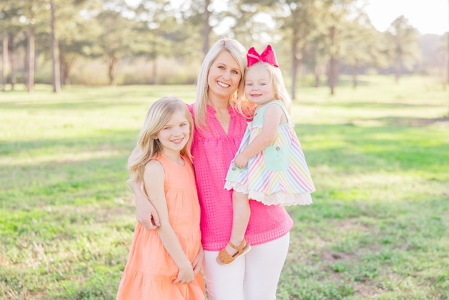 mom in pink shirt holds her daughters 